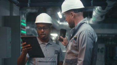 Genç fabrika uzmanlarından oluşan çok ırklı bir ekip tablet bilgisayar ve telefon kullanıyor. Modern fabrikada endüstriyel üretim teknolojisini tartışan profesyonel mühendisler. Ağır sanayi kavramı.
