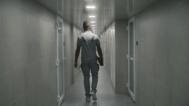 Üniformalı Afro-Amerikan profesyonel mühendis modern fabrika koridorlarında ya da tablet bilgisayar fabrikasında yürüyor. Endüstriyel tesisin ofis binasının koridorunda ağır sanayi işçisi var..