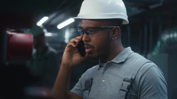 非裔美国人通过手机交谈 询问能源系统的设置 在现代重工业工厂或工厂从事安全制服和硬帽工作的专业工程师 — 图库视频影像