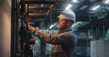 Güvenlik üniforması giyen, koruyucu gözlük takan ve boru hattını kontrol eden erkek ağır sanayi işçisi. Mühendis modern imalat fabrikası veya endüstriyel tesis işletiyor. Sanayi kavramı.