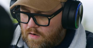 Gözlüklü ve kulaklıklı bir erkek müzisyenin MIDI klavye çalmasını, müzik bestelemesini ve dışarıda ritmik bir şekilde oturmasını. Kafkasyalı adam dağlarda tatil yaparken yeni şarkılar kaydetti..