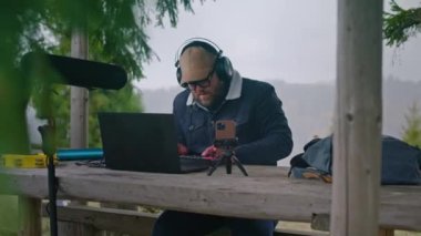 Beyaz adam müzik bestelemek için dijital elektrikli piyano kullanır. Yetişkin müzisyen çardakta müzik aletleriyle oturuyor, telefon tripod ve dizüstü bilgisayarda, ritmik olarak hareket ediyor ve açık havada şarkı yaratıyor..