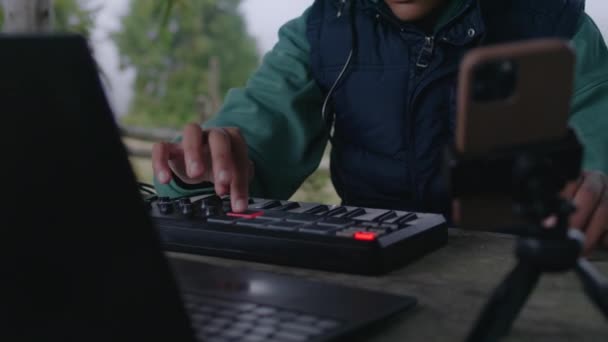 非洲裔美国音乐家在室外的Midi控制器上演奏 年轻的作曲家创作并记录音乐 在三脚架上使用笔记本电脑和电话 一边坐在加泽博一边 一边掌握新的歌曲 靠近点慢动作 — 图库视频影像