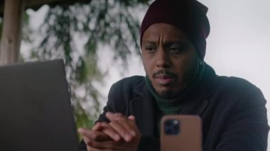 Afro-Amerikalı iş adamı tripodun üzerinde telefonla konuşuyor. Gezgin, güzel ormanda tatil sırasında iş ortaklarına uzaktan danışıyor. Açık havada çalışmak.
