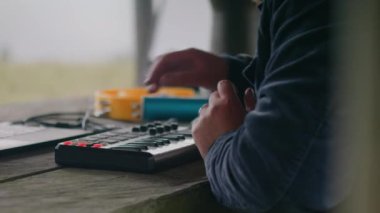 Kafkasyalı müzisyenlerin kulaklıklarıyla dijital elektrikli piyano çalarken, ritmik hareket ederken ve çardakta müzik yaratırken. Adam dağlarda tatil yaparken şarkı kaydetmek için dizüstü bilgisayar kullanıyor..