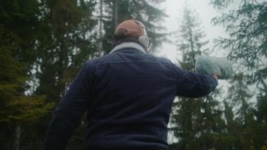 Kulaklık takan ses tasarımcısı, kozalaklı ormanda film için doğanın sesini kaydediyor. Kürklü ön cam mikrofon kullanıyor. Beyaz adam dışarıda profesyonel ses ekipmanlarıyla çalışıyor. Yavaş çekim.