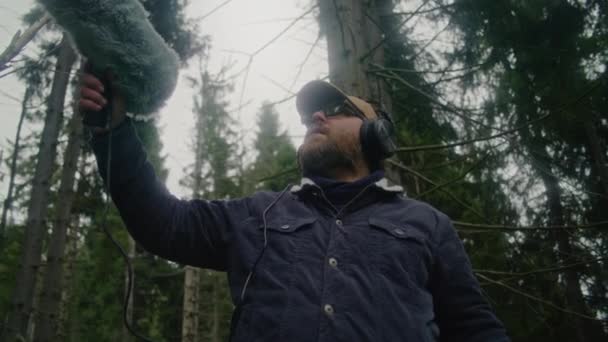 Kulaklık Takan Erkek Gezgin Profesyonel Ses Ekipmanları Kullanarak Kozalaklı Ağaçlarda — Stok video