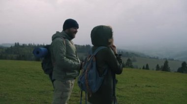 Sırt çantalı ve yürüyüş direkli bir çift yürüyüşçü güzel tepenin üstünde duruyor. Turist ailesi uzun bir yolculuk ya da dağ gezisinden sonra dinlenmek için durdu. Doğa keşfi ve turizm kavramı.