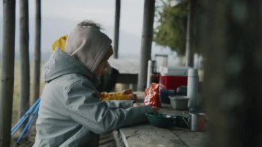 Genç çocuk ailesiyle masada oturur ve kese içinde yiyecek taşır. Bir grup turist uzun bir yürüyüşten sonra çardakta dinleniyor. Sonbaharda dağlara yolculuk yapan yürüyüşçüler. Açık hava eğlencesi.