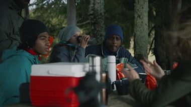 Bir grup turist uzun bir yürüyüşten sonra ahşap çardakta oturur, konuşur ve çay içerler. Çok ırklı yürüyüşçüler ya da gezginler sonbaharda dağ yürüyüşü sırasında dinlenirler. Etkin yeniden yaratma.