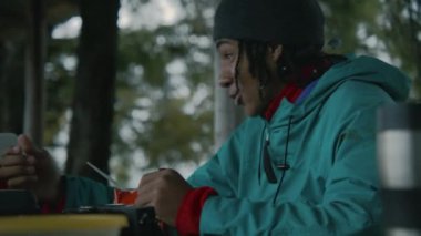 Genç Afrikalı Amerikalı turistlerin yürüyüş arkadaşlarıyla konuştuğu ve kese içinde yürüyüş yapan yiyecekleri yediği yakın plan. Genç, uzun bir yürüyüşten sonra çardakta dinleniyor. Sonbaharda dağlarda gezinti yapan gezgin.