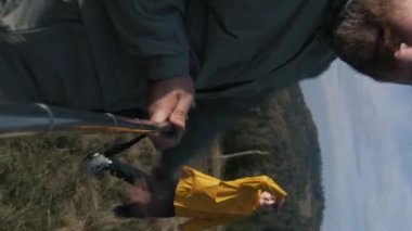Telefon kamerasından POV. Yetişkin bir adam, kızlarıyla birlikte dağ başında yürüyüş yaparken ya da yürüyüş yaparken videolar kaydeder. Yürüyüşçülerin ya da gezginlerin mutlu ailesi kamera önünde el sallıyor. Dikey video.