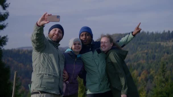 多民族旅行者のグループは 丘の上に立っている自然の風景の前に電話でセルフィーを取ります ハッピーな友人や山での休暇中に仲間をハイキング アクティブレクリエーション — ストック動画