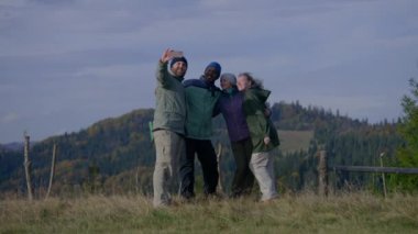 Mutlu çok ırklı arkadaşlar ya da yürüyüş arkadaşları tepenin üstünde duran güzel manzaranın önünde telefonla selfie çekiyorlar. Dağlarda seyahat ederken bir grup turist. Açık hava aktiviteleri.