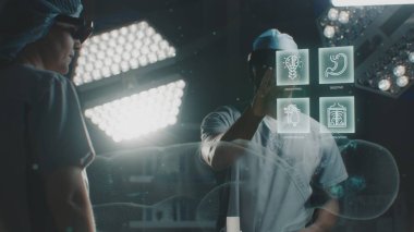 AR kulaklıklı çeşitli cerrahlar ameliyathanede çalışıyor. Afrikalı Amerikalı uzman, insan iskeleti ve organlarının 3 boyutlu animasyonuyla sanal holografik görüntü kullanıyor. Yapay zeka destekli ameliyat teknolojisi..
