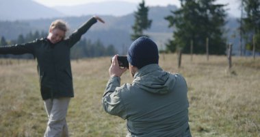 Beyaz bir adam profesyonel kamera kullanarak karısının tepede doğa manzarasına karşı fotoğraflarını çekiyor. Bir çift gezgin, dağ yürüyüşü sırasında turist ailesi. Aktif boş zaman.