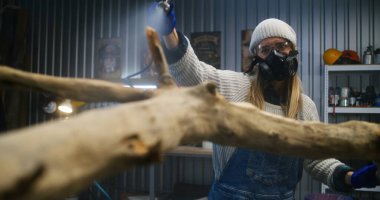 Solunum cihazındaki kadın marangoz ağaç dalına sıvı veya ahşap cila sıkar. Kadın esnaf ya da tasarımcı, modern atölyede ahşap ürünler yapıyor. El işi ve girişimcilik kavramı.