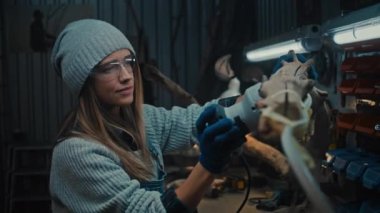 Sander kullanarak koruyucu gözlük takan yaratıcı kadın marangoz. Genç kadın marangozluk, şık bir atölyede ahşap ürünler yapıyor. El yapımı ve küçük işletme konsepti.