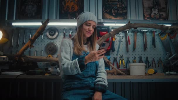 Kvindelig Tømrer Håndværker Bruger Mobiltelefon Sidder Stilfuldt Værksted Træ Produkt – Stock-video