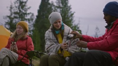 Çok ırklı turist grubu ormanda kamp kuruyor. Yürüyüş arkadaşları kampta oturur ve konuşurlar. Afrikalı Amerikalı adam beyaz kadın için çay dolduruyor. Yürüyüşçüler dağlarda tatil yaparken dinlenirler..