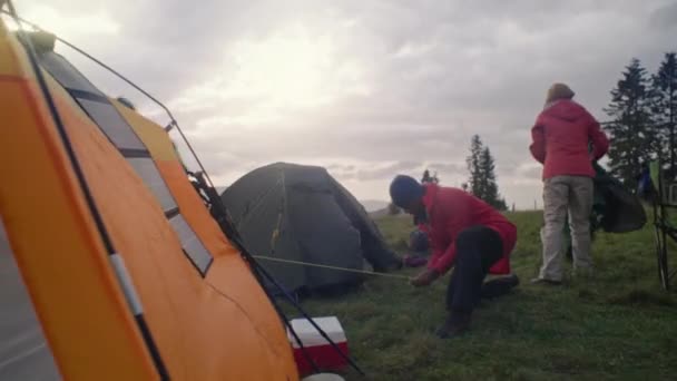 多民族旅行者のグループは 長い遠征の後 キャンプ場で休憩するために停止します 観光客はテントをセットアップし 寝袋をレンタルする 休暇中のアウトドアファン 自然発見の概念 — ストック動画