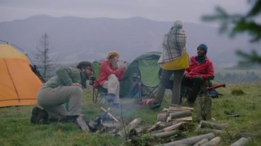 Çok ırklı turist grubu ormandaki kampta dinleniyor. Beyaz adam kamp ateşi yaktı. Yetişkin bir kadın oturur, yürüyüş arkadaşlarıyla konuşur ve telefonda fotoğraf çeker. Yürüyüşçüler dağlara giderken.