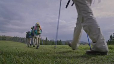 Sırt çantalı ve yürüyüş direkli bir grup yürüyüşçü güzel bir dağ tepesinde patika boyunca yürür. Turistler inanılmaz doğa manzaraları keşfeder. Aktif eğlence ve açık hava keşfi kavramı. Düşük açı.