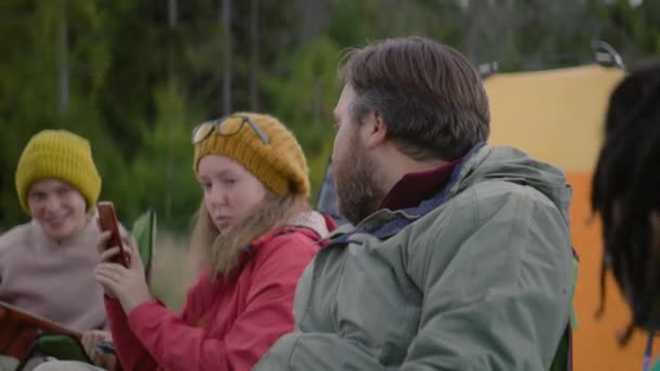 在森林里的营地里休息着各种各样的远足伙伴 成年妇女在手机上拍照 白人男人坐在那里和朋友们交谈 旅游团在山中度假 — 图库视频影像