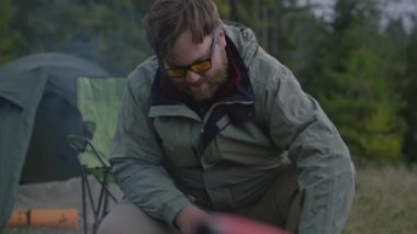 Yetişkin beyaz bir adamın kamp ateşi yakması ve odun ateşlemesi. Bir grup turist ormanda kamp kurdular. Yürüyüşçüler dağlara yaptıkları gezi sırasında dinlenirler. Turizm ve aktif eğlence kavramı.