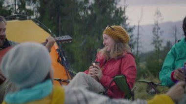 Çeşitli turist grupları kamp ateşinin yanında dinleniyor ve müzik dinliyor. Yetişkin beyaz adam şarkı söyler ve gitar çalar. Yürüyüş arkadaşları çay içer, konuşur ve güler. Dağlara gezintiye çıkan yürüyüşçüler.