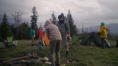 Çok ırklı gezginlerden oluşan bir grup, uzun bir yolculuktan sonra dinlenmek için kamp alanında mola veriyor. Turistler çadır kurar, odun keser ve ateş yakar. Tatildeki açık hava meraklıları. Doğa keşfi ve aktif eğlence.