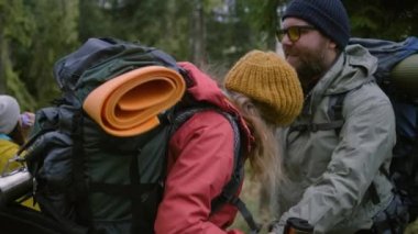 Gözlüklü turist kadın yürüyüş arkadaşına sırt çantasını çıkarmasında yardım eder, su içmeye başlarlar. Bir grup gezgin ormanda uzun bir yolculuktan sonra dinlenmek için durdu. Doğa keşfi ve aktif eğlence.