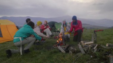 Bir grup turist tepedeki kampta dinleniyor. Yetişkin yürüyüşçüleri olan gençler kamp ateşinde marshmallow pişiriyor. Beyaz adam gitarla oturuyor. Dağlara seyahat eden gezginler.