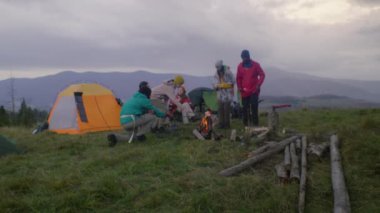 Bir grup turist tepedeki kampta dinleniyor. Yürüyüşçüler kamp ateşinde marşmelov pişirir. Beyaz adam oturur, yer ve bir kadınla konuşur. Dağlarda yürüyüş arkadaşları..
