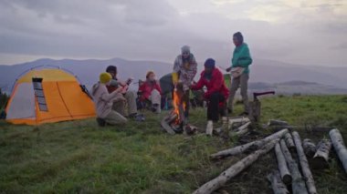 Çok ırklı gezginlerden oluşan bir grup kamp alanında dinlenmek için durdu, ateş yakıp yemek pişirmeye başladılar. Turistler yürüyüş sırasında gitar çalar, konuşur ve birlikte yemek yerler. Doğa keşfi ve turizm kavramı.