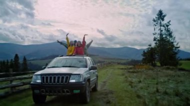 Bir grup turist birlikte dağlarda tatile çıkıyor. Yürüyüşçüler arabanın sunroof 'unda ayağa kalkar, güler ve el sallarlar. İnsanlar araba gezisinde eğleniyor. Açık hava meraklıları.
