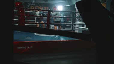 Boks eldivenli kadın boksör, erkek antrenörle dövüş tekniği uyguluyor ve karanlık spor salonunda turnuvaya hazırlanıyor. Atletik boksör boks ringinde yumruk tokuşturuyor. Fiziksel aktivite ve egzersiz.