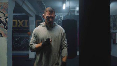 Boks bandajlı erkek boksör trenler ve kum torbasına çarpıyor. Sporcu adam egzersiz yapar, dövüş teknikleri uygular ve yarışmaya hazırlanır. Fiziksel aktivite ve yoğun çalışma.