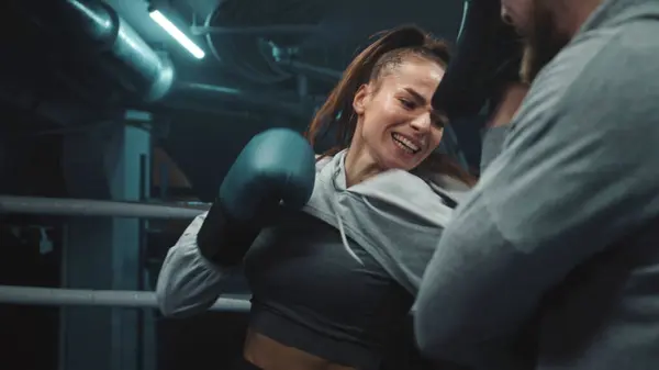 Close up of female fighter in boxing gloves practicing fighting technique and exercising before match in gym. Athletic boxer hits punching mitts on boxing ring. Physical activity and workout concept.