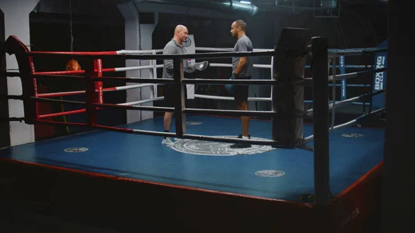 African American fighter in boxing gloves stands on ring and talks with trainer. Caucasian coach explains fighting techniques and consult boxer before competition. Physical activity and workout.