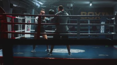 Boks eldivenli kadın boksör, erkek antrenörle dövüş tekniği uyguluyor ve şampiyonluktan önce karanlık spor salonunda egzersiz yapıyor. Boksör boks ringinde yumruk tokuşturuyor. Fiziksel aktivite ve egzersiz.
