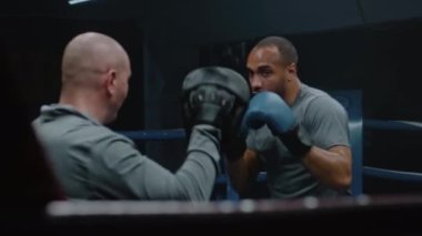 Boks eldivenli Afrikalı Amerikalı boksör boks müsabakasından önce antrenörle boks ringinde egzersiz yapıyor. Sporcu, spor salonunda yumruk yumruğa antrenman yapar. Fiziksel aktivite ve yoğun çalışma.