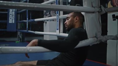 Yorgun ve yorgun Afrikalı Amerikalı boksör boks ringinin köşesinde oturuyor. Yüzünde boncuk boncuk ter olan dövüşçü antrenmandan sonra dinleniyor. Sporcu boks salonunda turnuvaya ya da yarışmaya hazırlanıyor. Dolly vurdu..