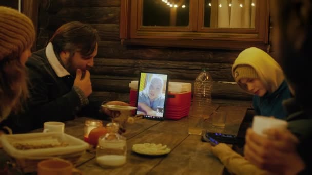 晚上吃饭的时候 一群游客坐在桌旁 用平板电脑通过视频聊天与女人交谈 多民族朋友周末在乡间度假别墅附近休息 — 图库视频影像
