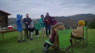 İki adam barbekü ızgarasının yanında çocuklarla dans edip eğleniyor. Kadınlar çimde kamp sandalyelerinde otururlar. Dağlardaki tatil gezisi sırasında dışarıda dinlenen çok ırklı bir arkadaş grubu. Aktif boş zaman.