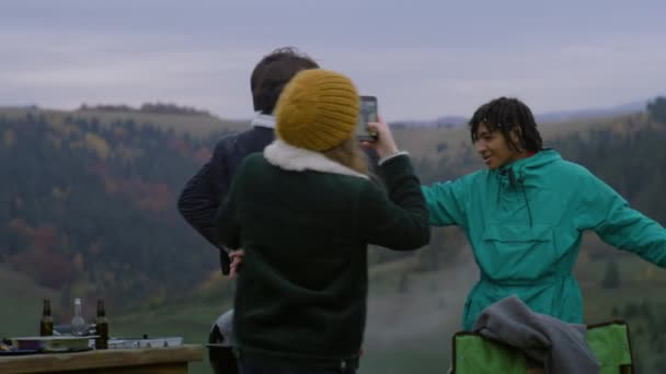 在烧烤晚餐期间 白人男子与非洲裔美国少年跳舞 女人在手机上拍摄视频 在山中旅行时 多民族的旅游朋友或家人在屋外玩得很开心 — 图库视频影像