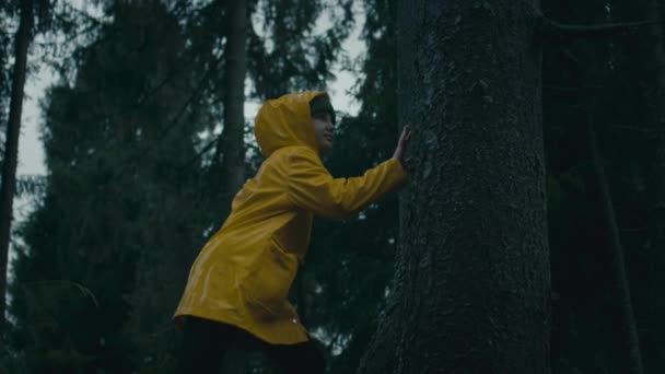 黄色いレインコートの若い観光客のシネマティックショットは 山でハイキングしながら雨林を歩いています 女の子は木に触れ 森で自然を楽しんでいる アウトドアレクリエーション スローモーション — ストック動画