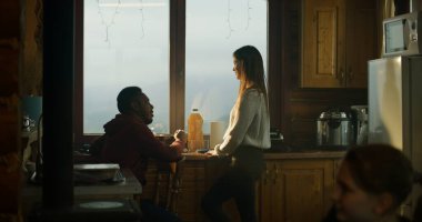 Çok ırklı bir turist çifti, yazlık mutfakta birlikte yemek pişiriyor. Afrikalı Amerikalı gençler ailelerine gelip buzdolabına bakıyorlar. Gezgin ailesi tatil sırasında ahşap kulübede dinlenmek için durdular..