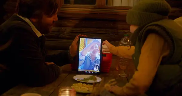 大人の男性は 子供と夕食中に屋外に座って ビデオ通話で女性と話している間 タブレットコンピュータを保持しています 田舎での休暇中に観光家族が一緒に休む — ストック写真