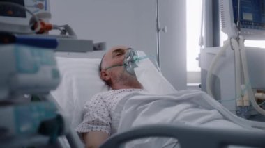 Oksijen maskeli kıdemli adam hastane koğuşunda yatıyor. Yapay akciğer solunum sırasında eski bir hasta. Klinikteki modern acil servis. Tıbbi tesiste yoğun bakım Coronavirus Bölümü.